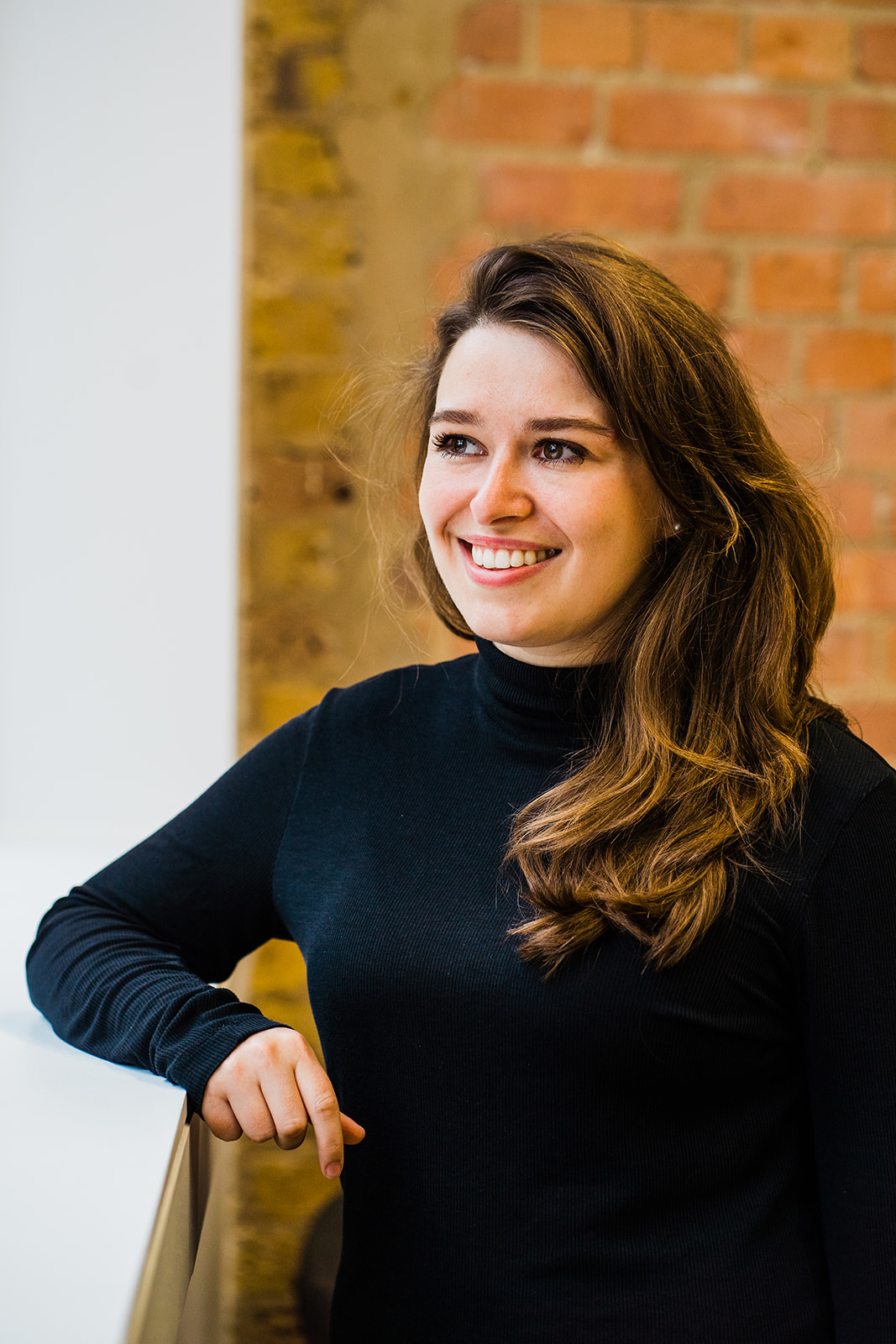 woman with long brown hair looks out of window and smiles for business head shot